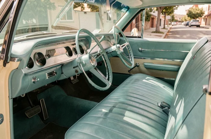 Intérieur restauré d'une Chevrolet Impala 1961 avec sa banquette vinyle turquoise, son tableau de bord chromé et son volant d'époque, vue depuis la portière ouverte